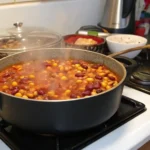 A pot of simmering calico beans on a stovetop.